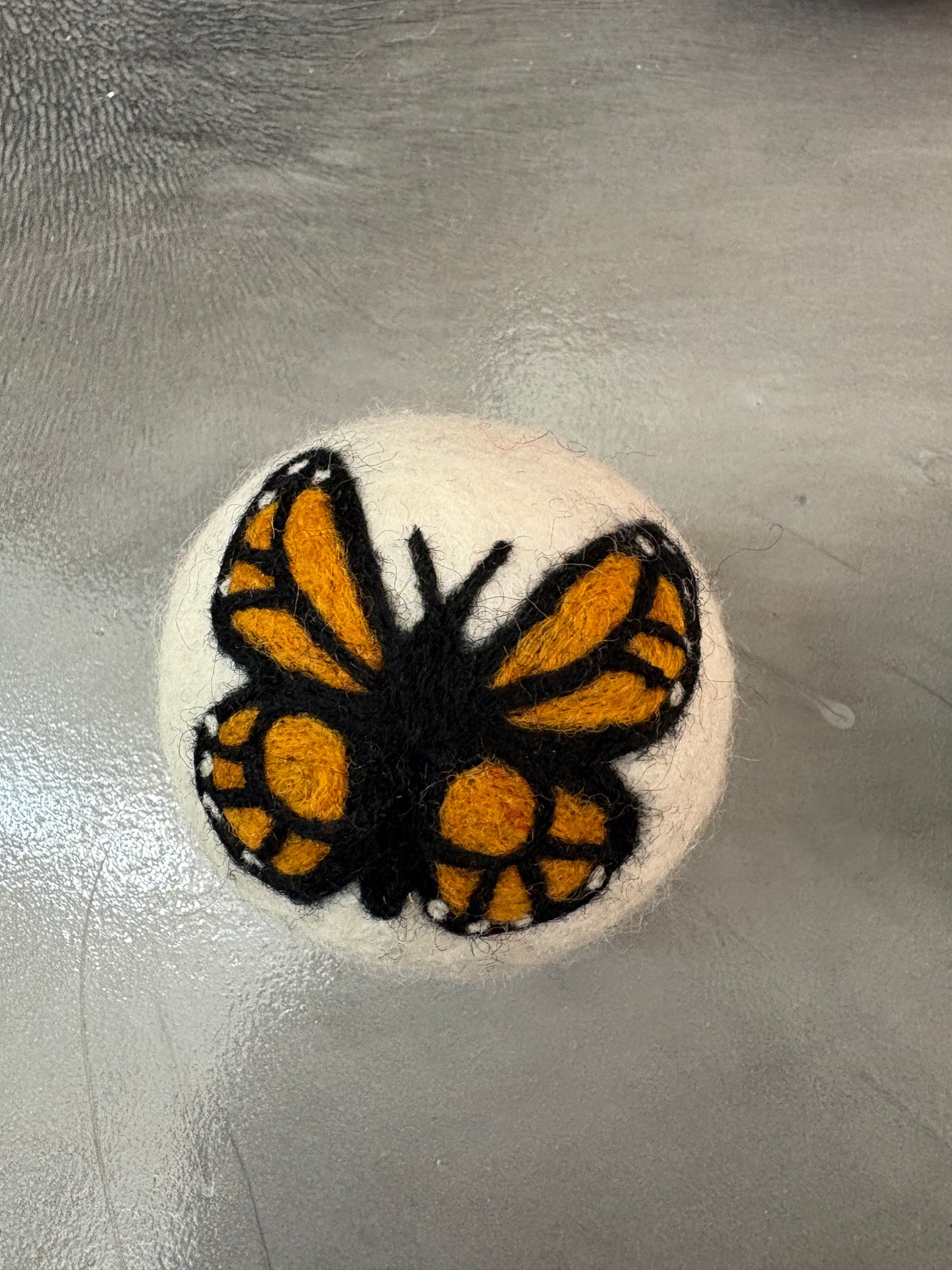white wool dryer ball with monarch butterfly design on a gray surface