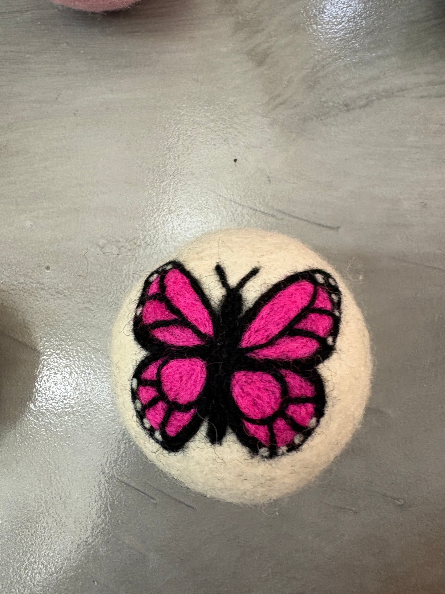 white wool dryer ball with a pink butterfly design on a metallic surface