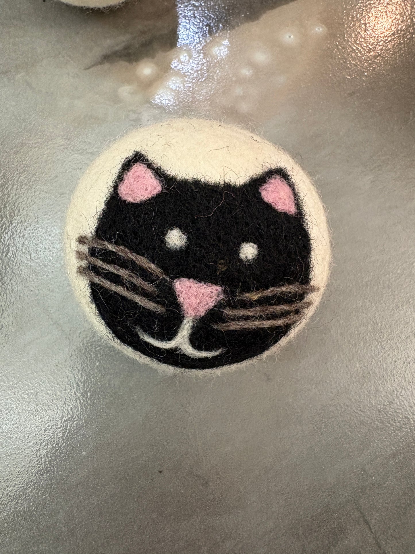 white wool dryer ball  with a black cat design on a metallic surface