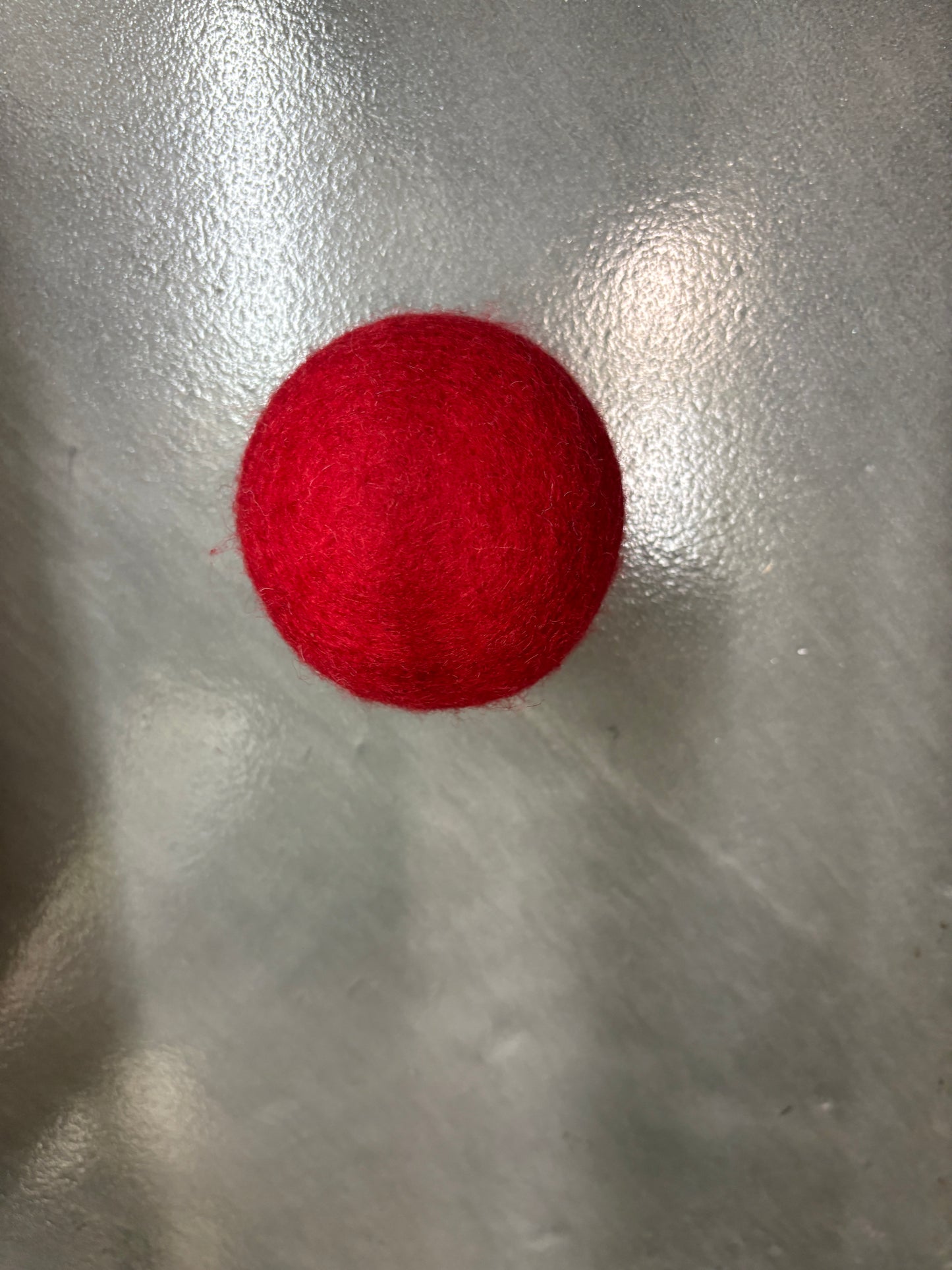Red wool dryer ball on a reflective silver surface