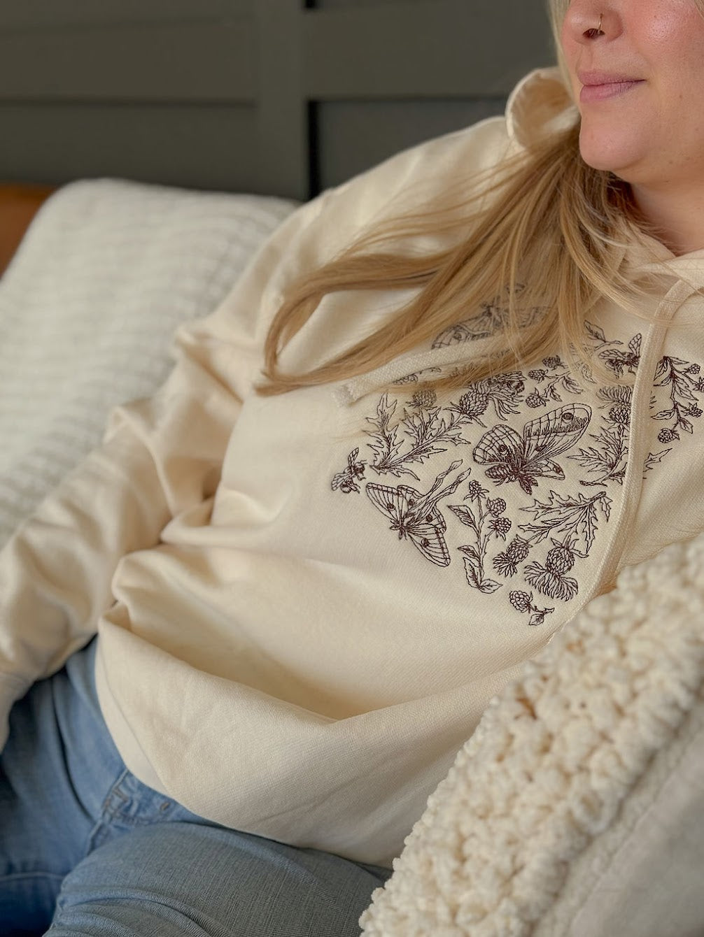 Person wearing a cream hoodie with butterfly design sitting on a couch.