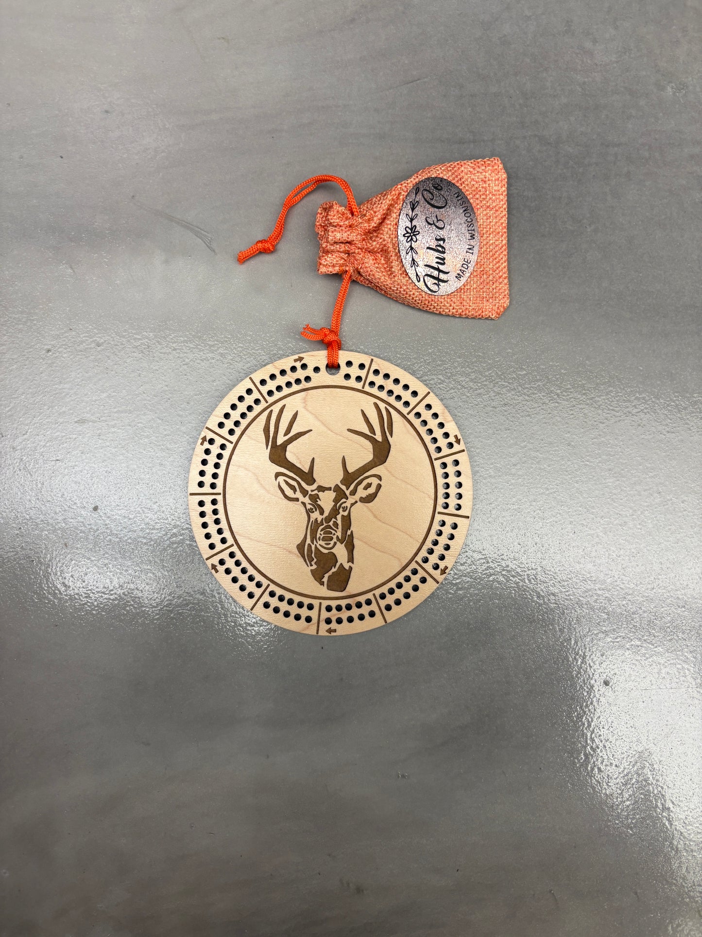 Decorative wooden cribbage board with deer design and drawstring pouch on a gray surface