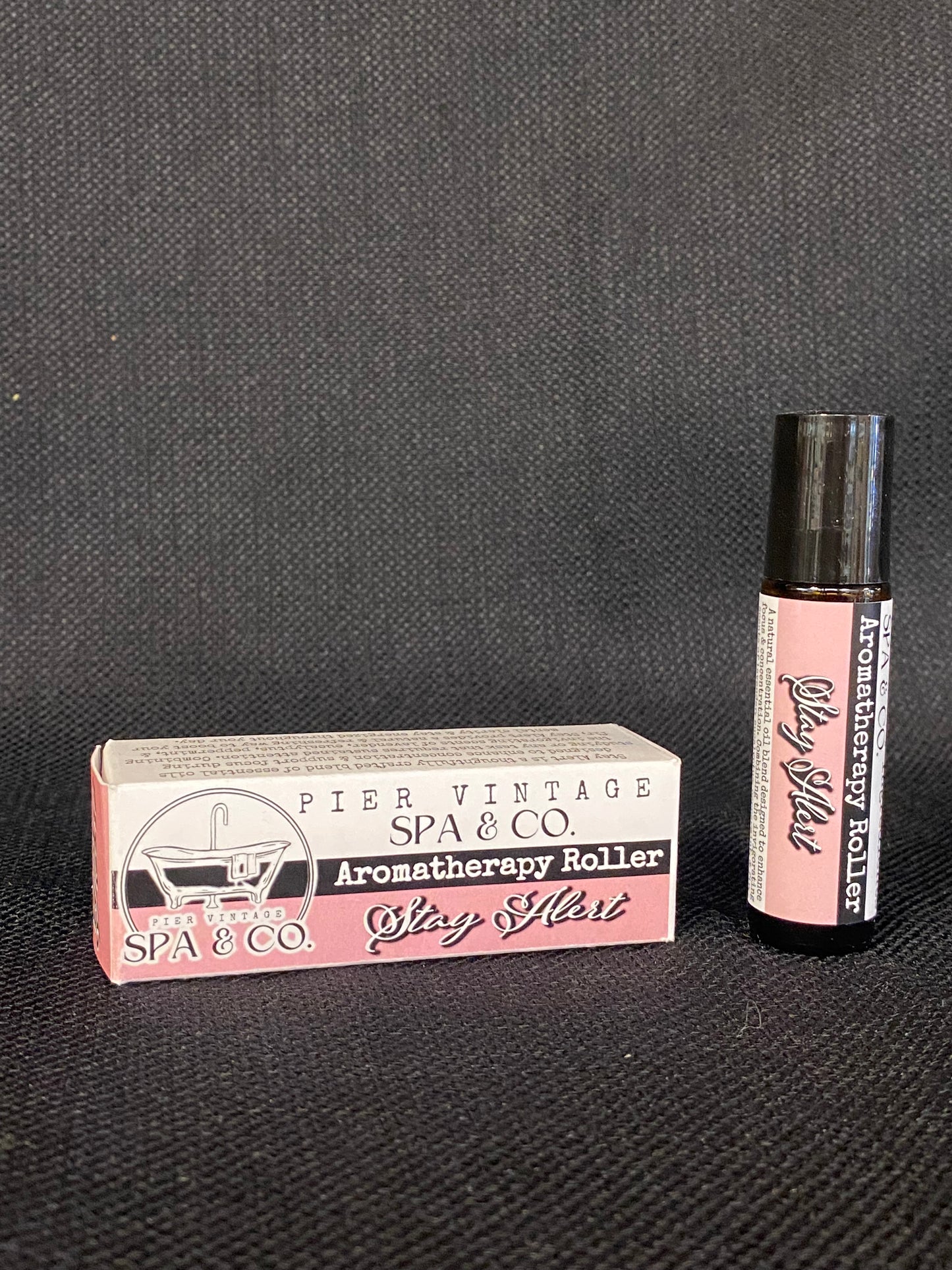 Aromatherapy roller with pink cap and white label on a dark textured background