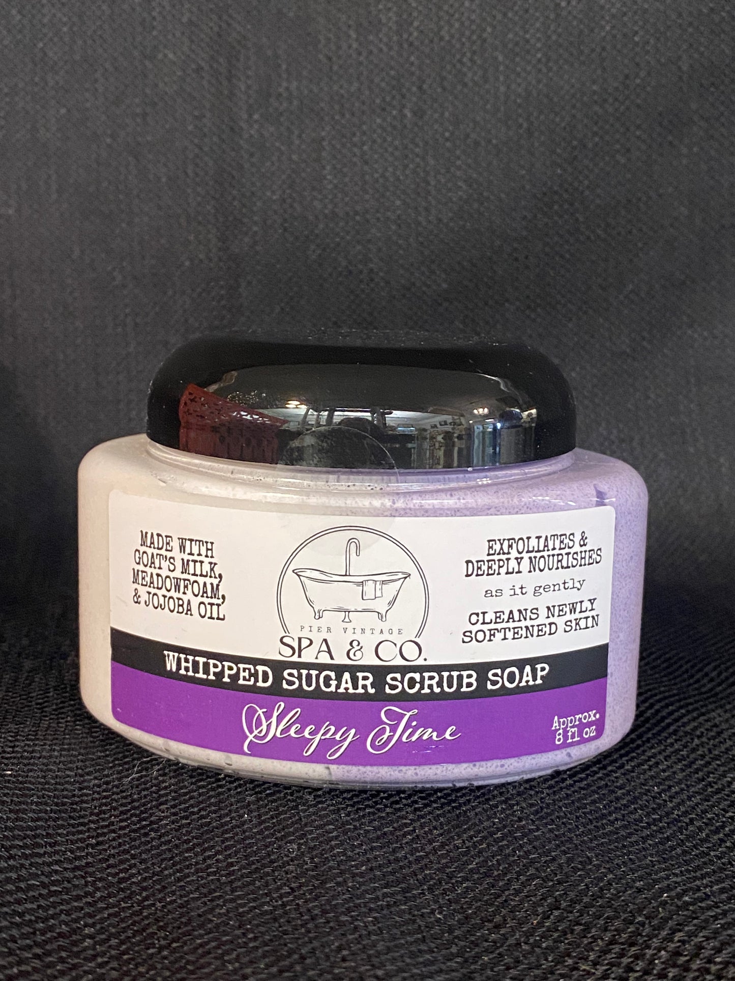 Jar of whipped sugar scrub soap with a purple and white label on a textured black surface from Pier Vintage Spa & Co.