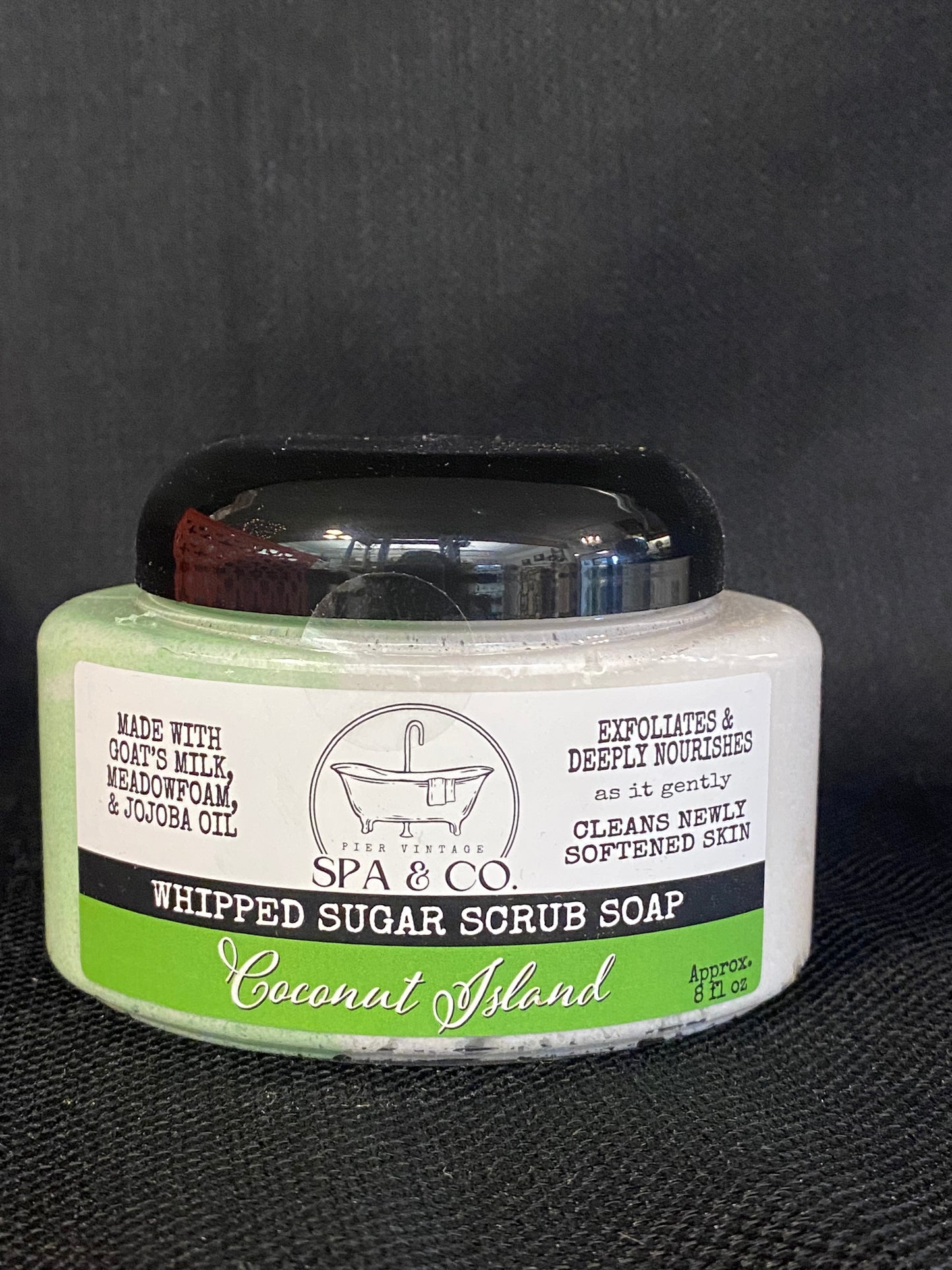 Jar of whipped sugar scrub soap with a green and white label on a textured black surface from Pier Vintage Spa & Co.