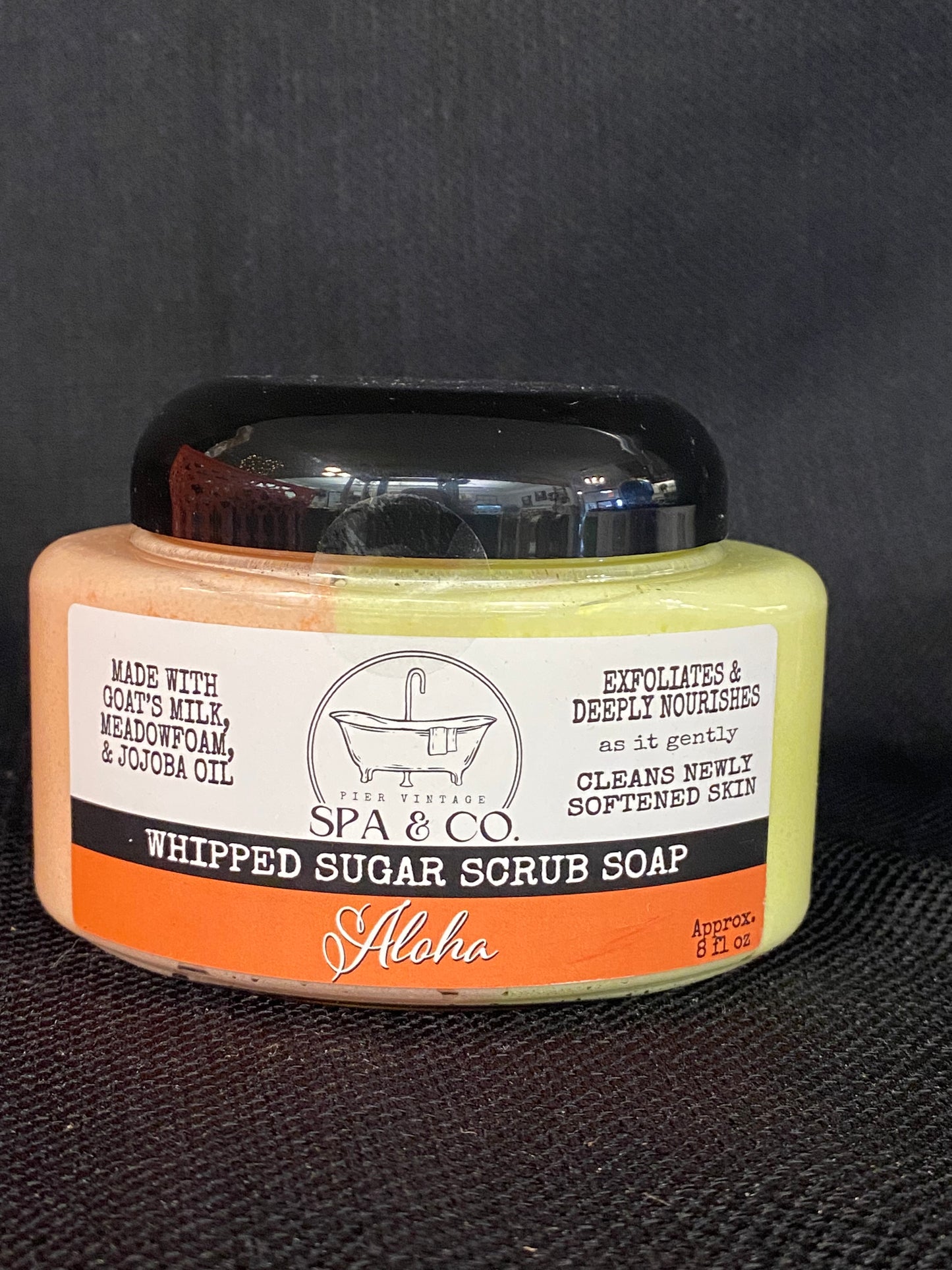 Jar of whipped sugar scrub soap with a orange and white label on a textured black surface from Pier Vintage Spa & Co.