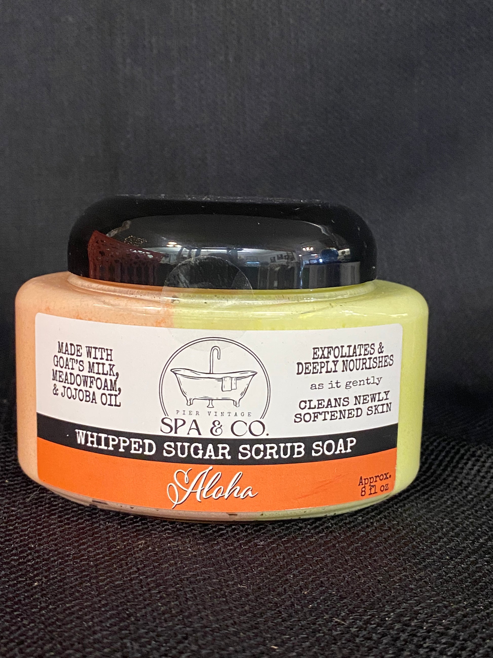 Jar of whipped sugar scrub soap with a orange and white label on a textured black surface from Pier Vintage Spa & Co.