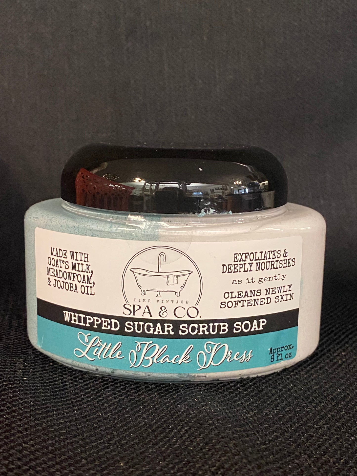 Jar of whipped sugar scrub soap with a blue and white label on a textured black surface from Pier Vintage Spa & Co.