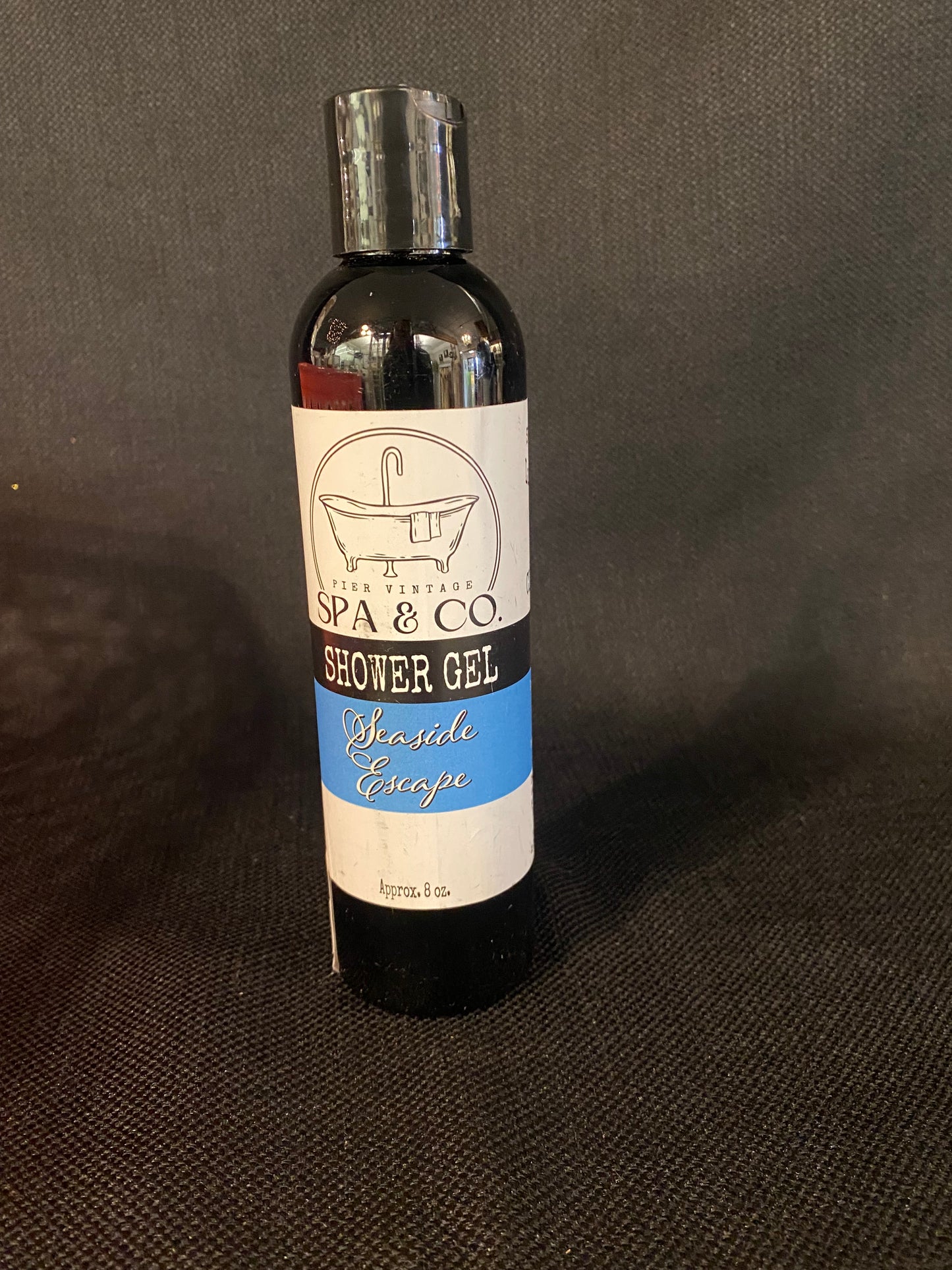 Bottle of Seaside Escape shower gel with a label on a dark textured surface by Pier Vintage Spa & Co.