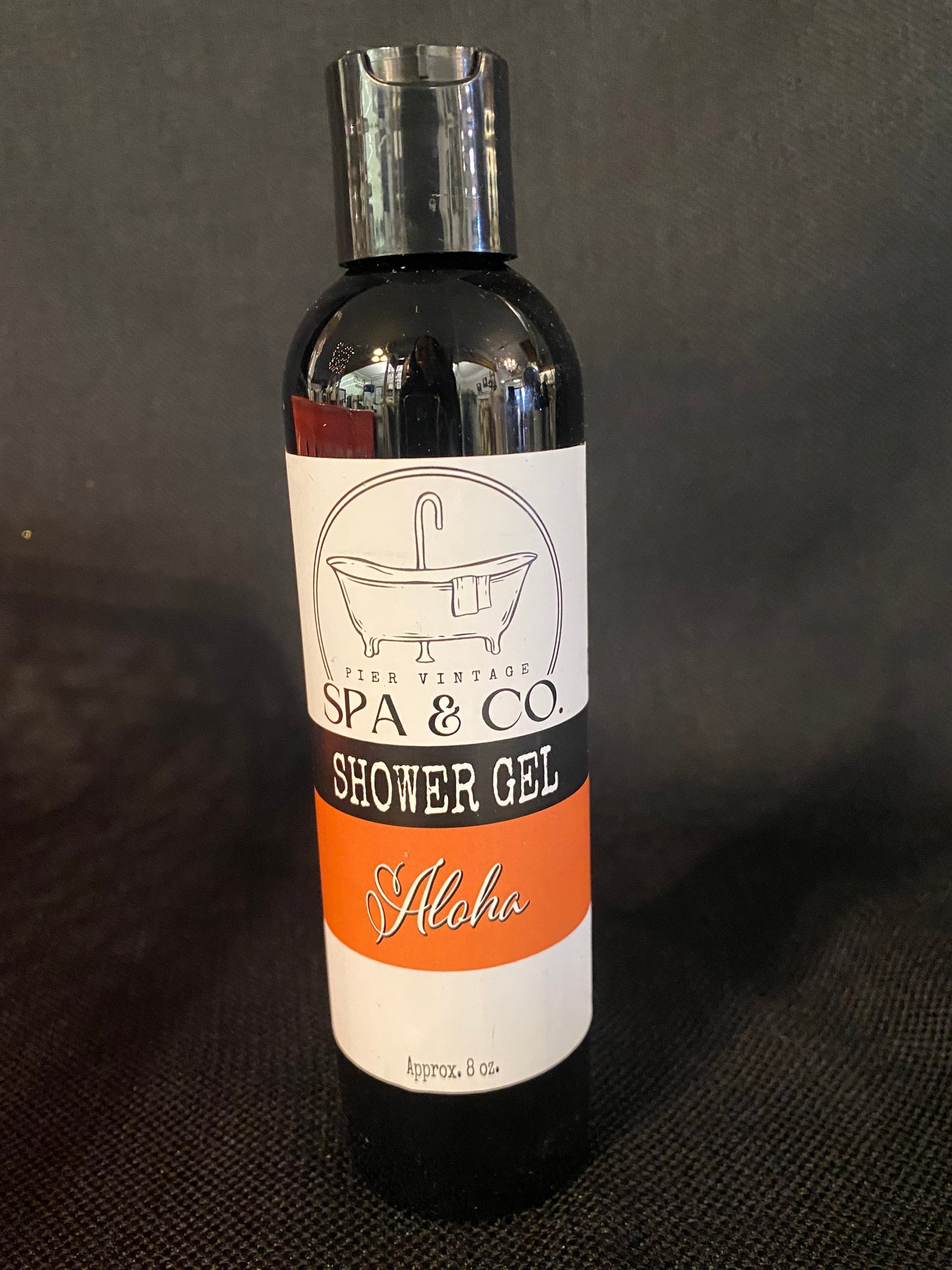Bottle of Aloha shower gel with a label on a dark textured background by Pier Vintage Spa & Co.