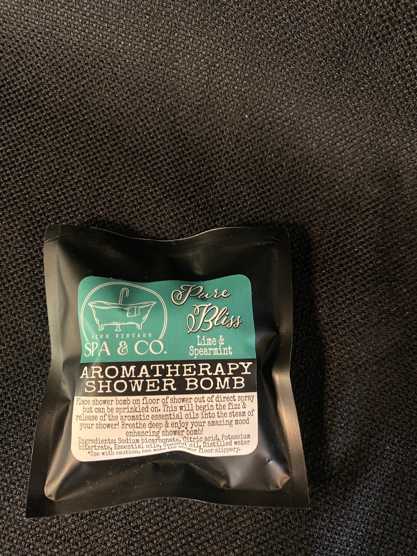 Packaged aromatherapy shower bomb with visible branding on a textured black surface