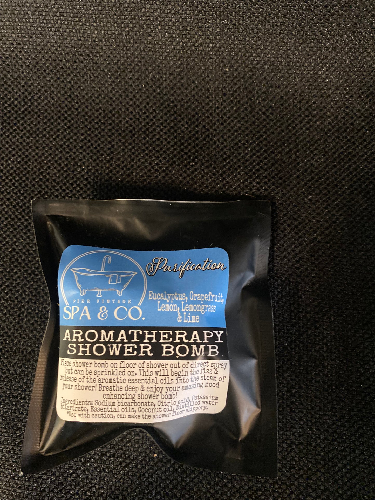 Packaged aromatherapy shower bomb with visible branding on a textured black surface