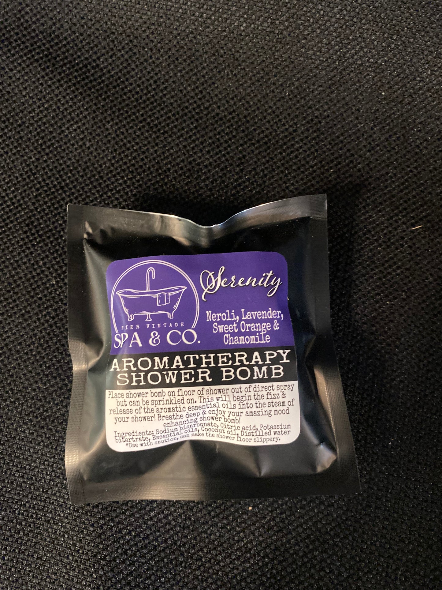 Packaged aromatherapy shower bomb with visible branding on a textured black surface
