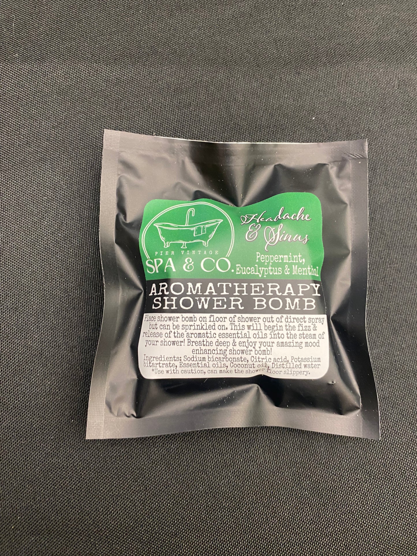 Packaged aromatherapy shower bomb with visible branding on a textured black surface