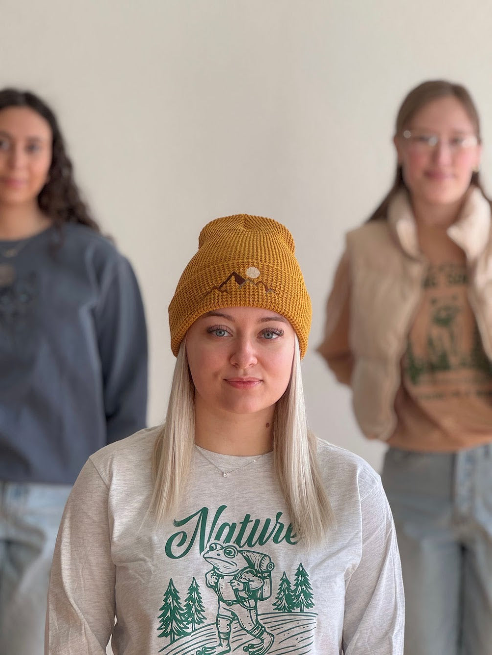 Embroidered Mountain Landscape on Mustard colored stocking hat on a woman in cream long sleeve standing with other women with white background