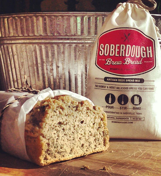 Roasted Garlic Soberdough bread loaf on wood counter with cloth bag and metal bucket in background
