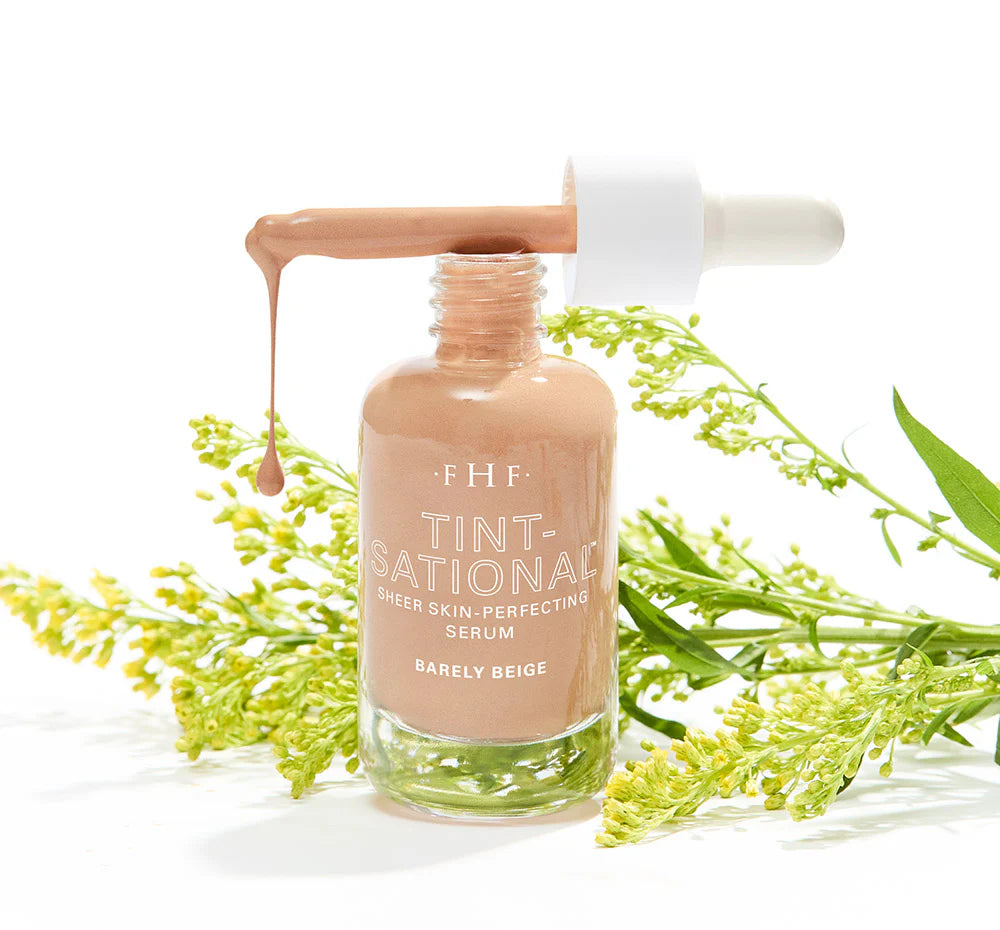 Bottle of FHF Tint-ational serum with dropper and green leaves on a white background