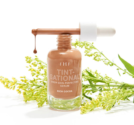 Serum bottle with dropper labeled 'FHF Tint-National' surrounded by green leaves on a white background