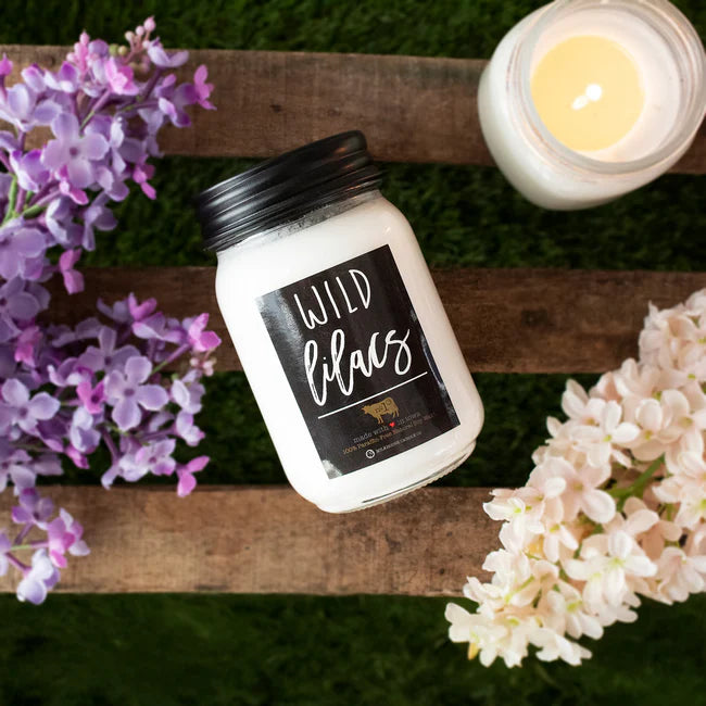 Scented candle labeled 'Wild Lilacs' with flowers on a wooden surface