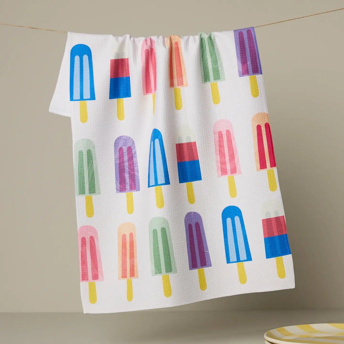 Geometry Tea Towel with colorful popsicle pattern hanging on a line against a beige background