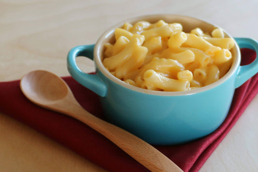 Blue bowl of macaroni and cheese with a wooden spoon on a red cloth