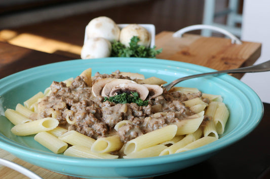 Pasta dish with ground meat, mushrooms, and herbs in a teal bowl on a wooden table.