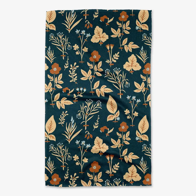 A rectangular kitchen towel with a dark teal background and a vintage botanical pattern featuring beige, rust orange, and light blue flowers and leaves, shown flat against a light gray background.