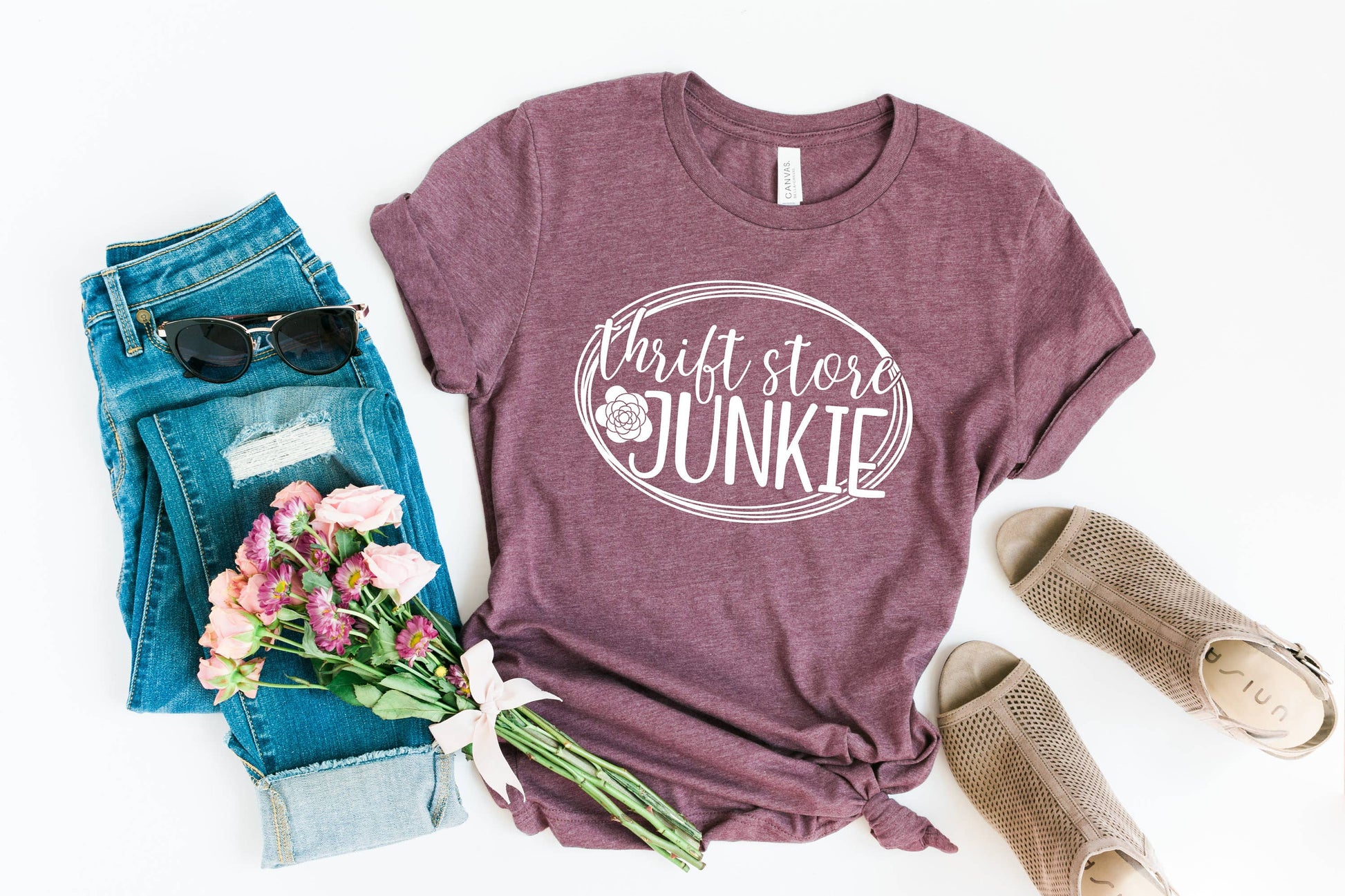 Maroon t-shirt with 'Thrift store Junkie' text, jeans, sunglasses, and flowers on a white background
