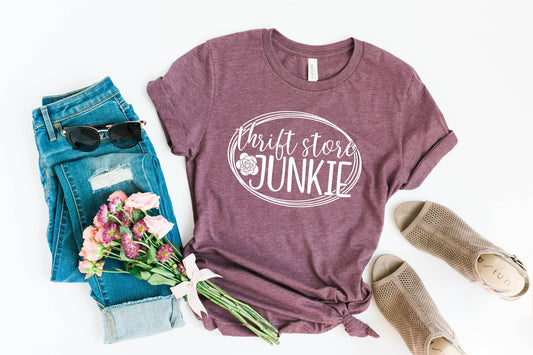 Maroon t-shirt with 'Thrift store Junkie' text, jeans, sunglasses, and flowers on a white background