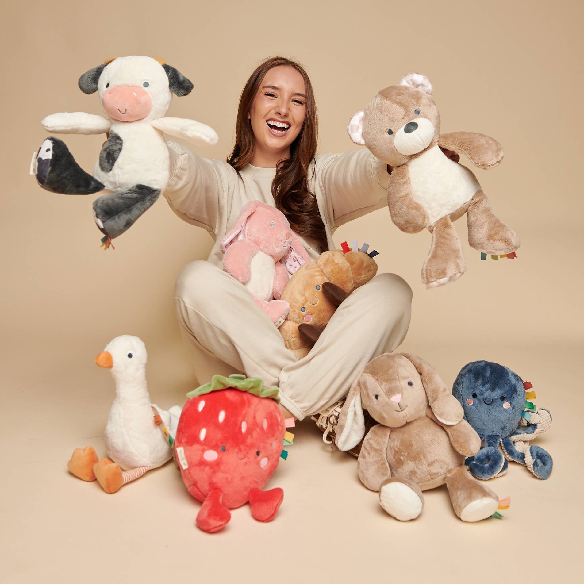 Woman holding and surrounded by various plush toys on a beige background