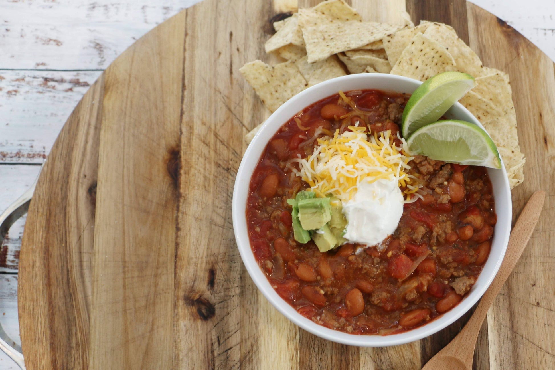 Bowl of chili with toppings on a wooden cutting board