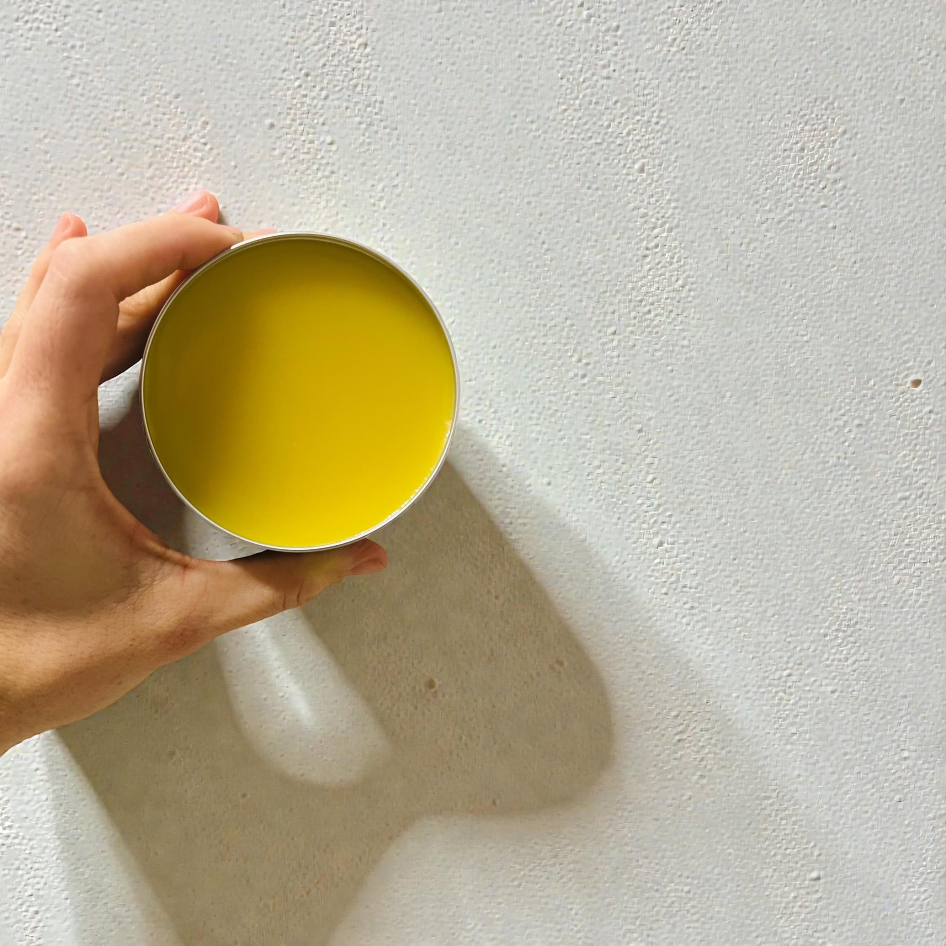 Hand holding a yellow beard balm container against a light gray background