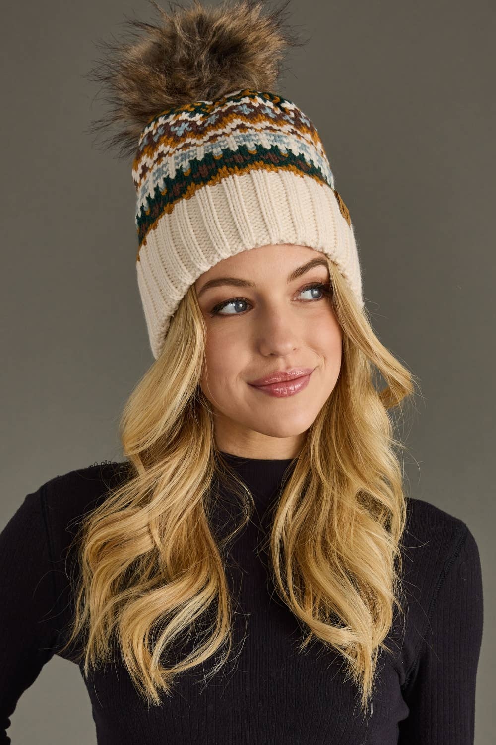 Woman wearing a patterned knit beanie with a pom-pom against a gray background