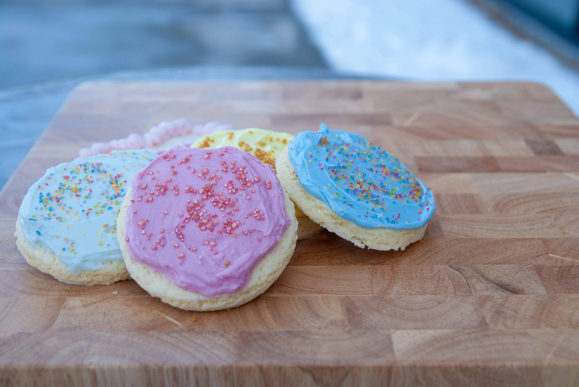 Three colorful cookies with sprinkles on a wooden cutting board.