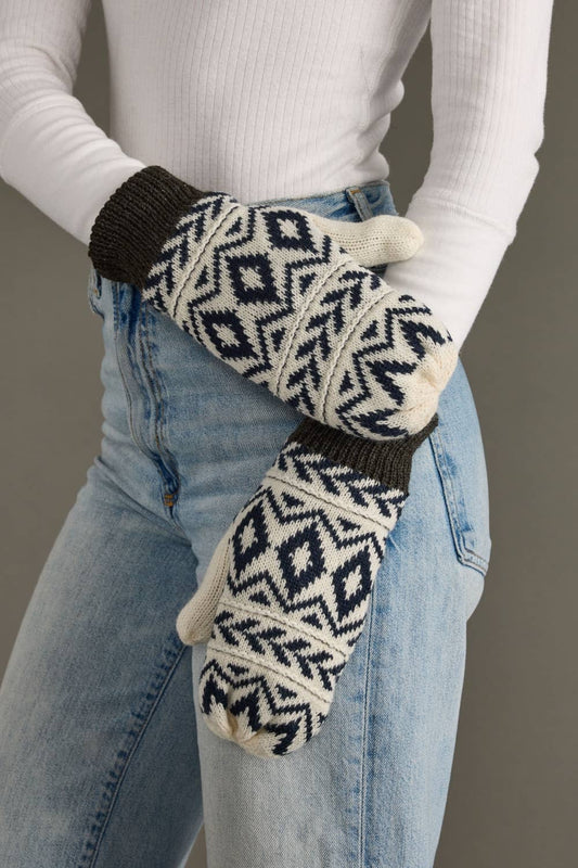 Person wearing navy and white patterned mittens with a gray cuff on a plain background