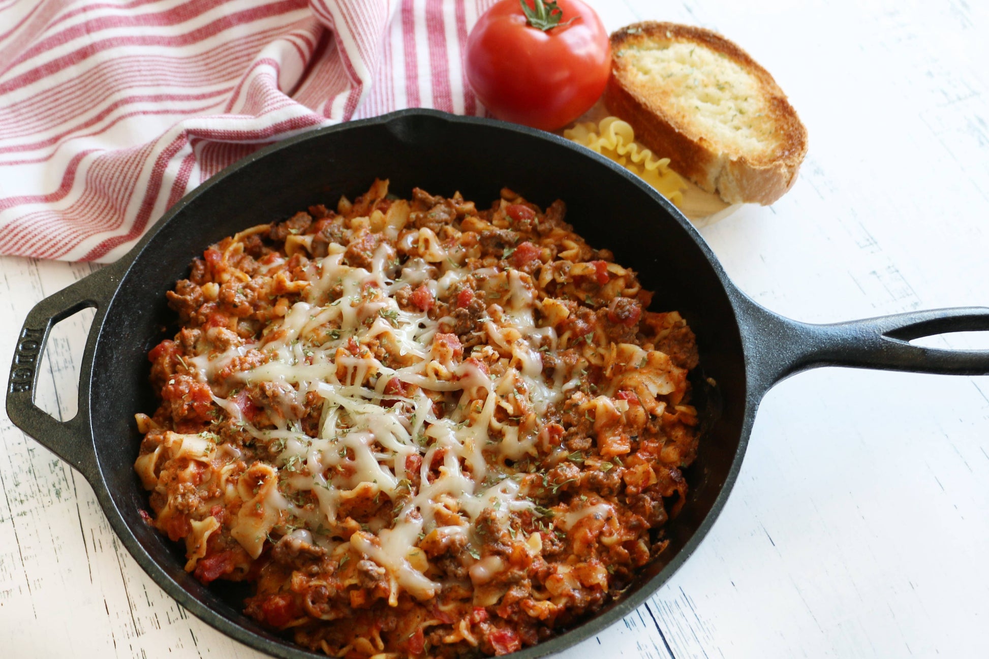 Skillet of pasta with tomato and bread on a white surface