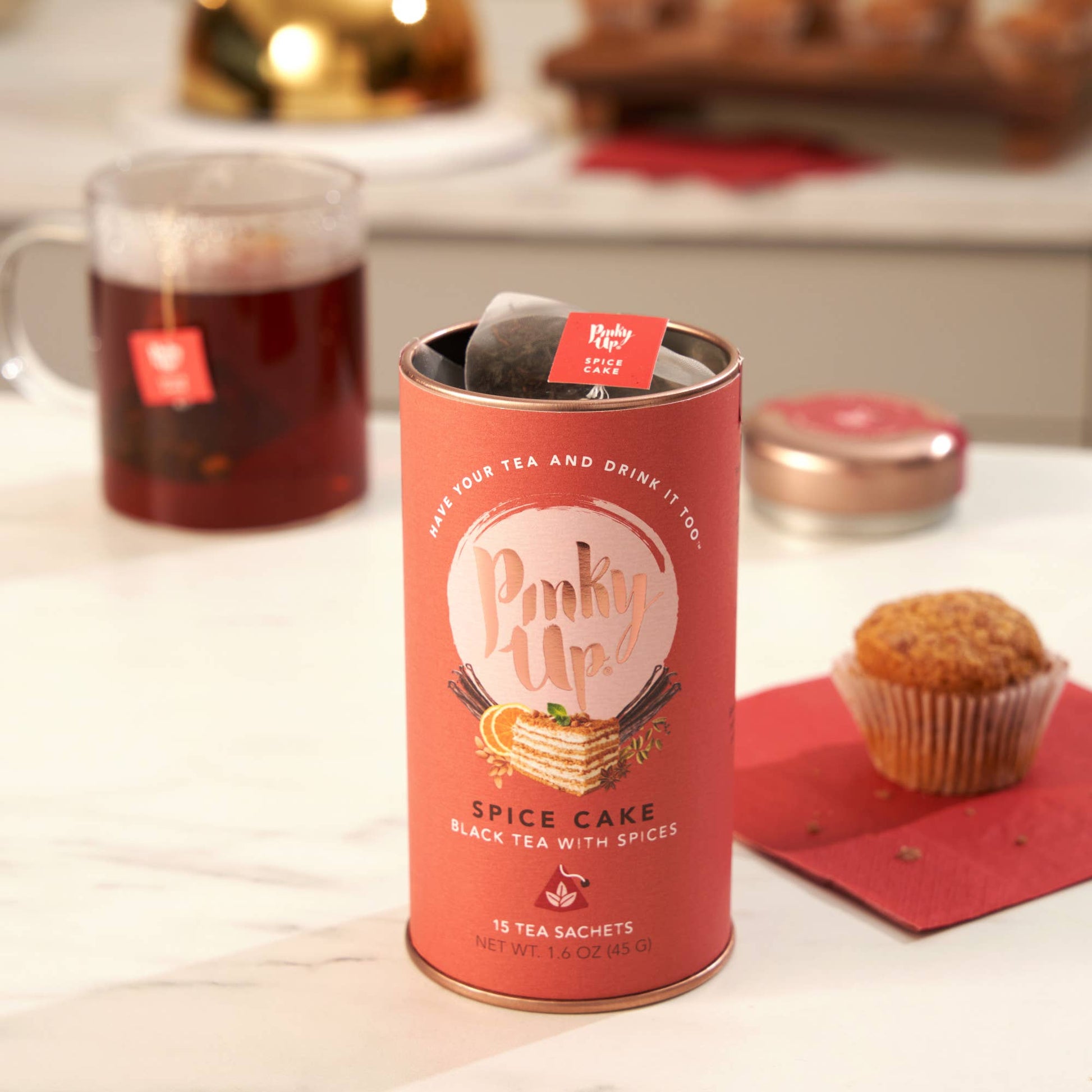 Pinky Up Spice Cake tea canister with a cup of tea and muffin on a table.