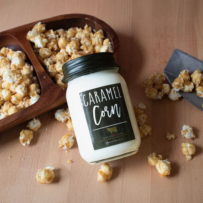 Jar of caramel corn with a wooden scoop and scattered popcorn on a wooden surface