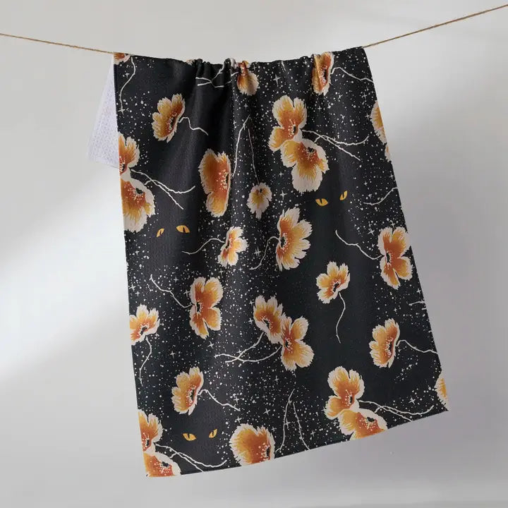 A Geometry tea towel with a floral print of orange, yellow, and white flowers, hanging from a thin string against a plain light gray background.