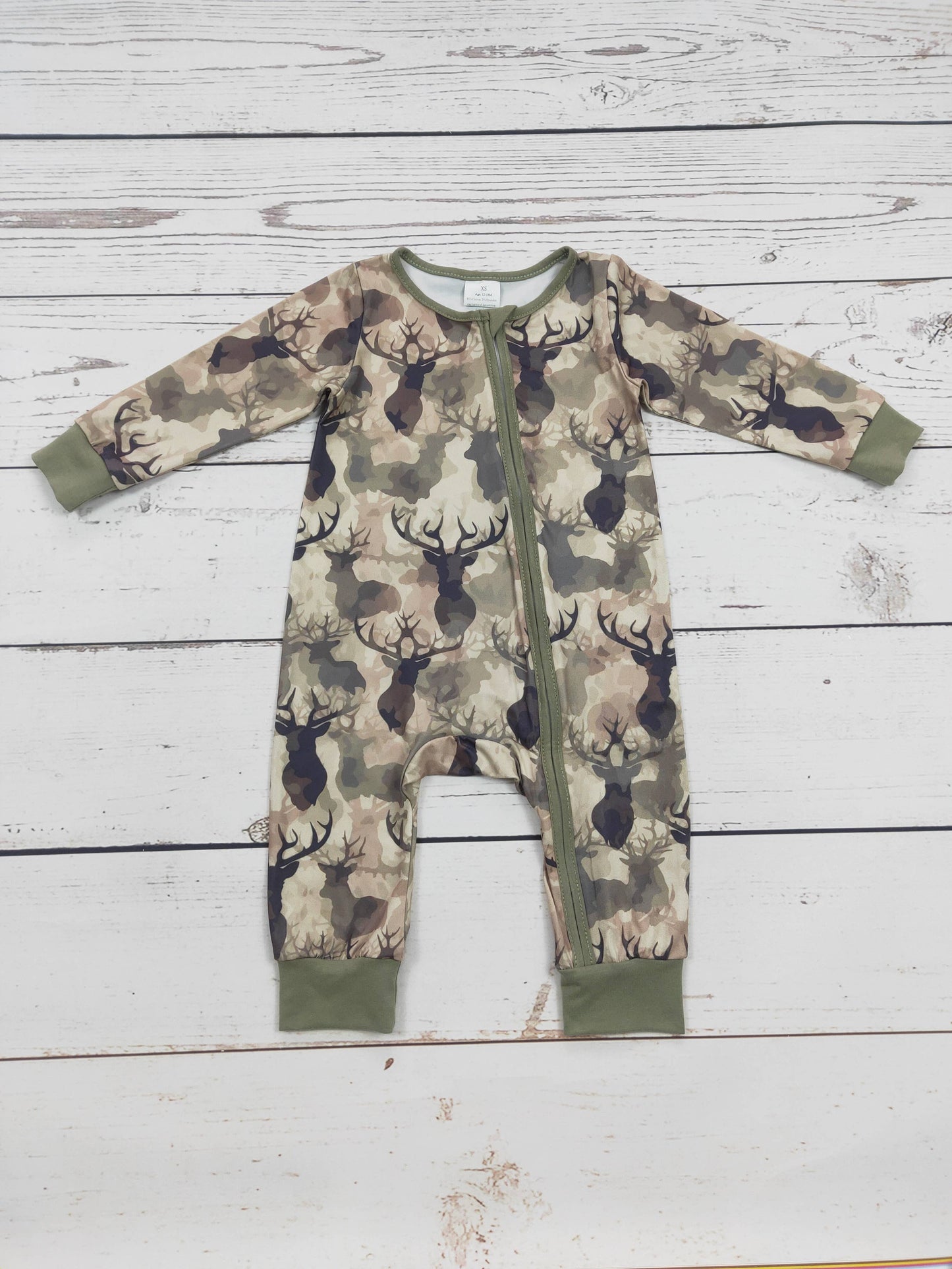 Camouflage-patterned baby romper with deer pattern with a zipper on a wooden surface