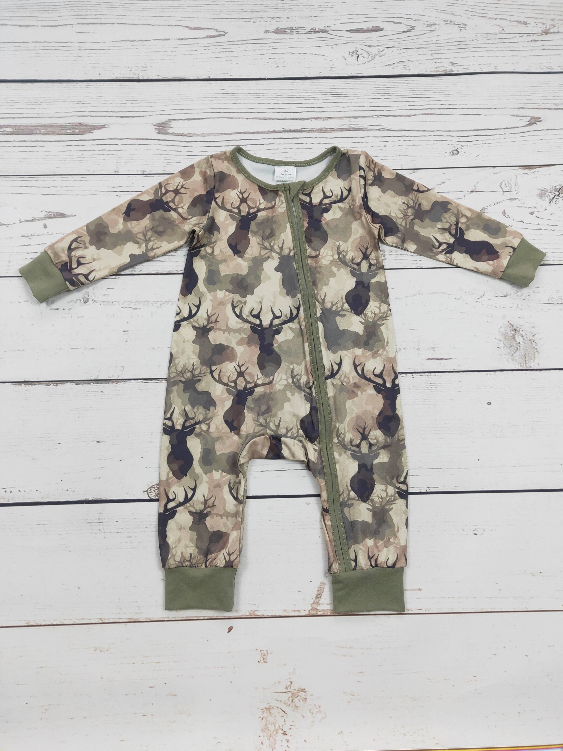 Camouflage-patterned baby romper with deer pattern with a zipper on a wooden surface