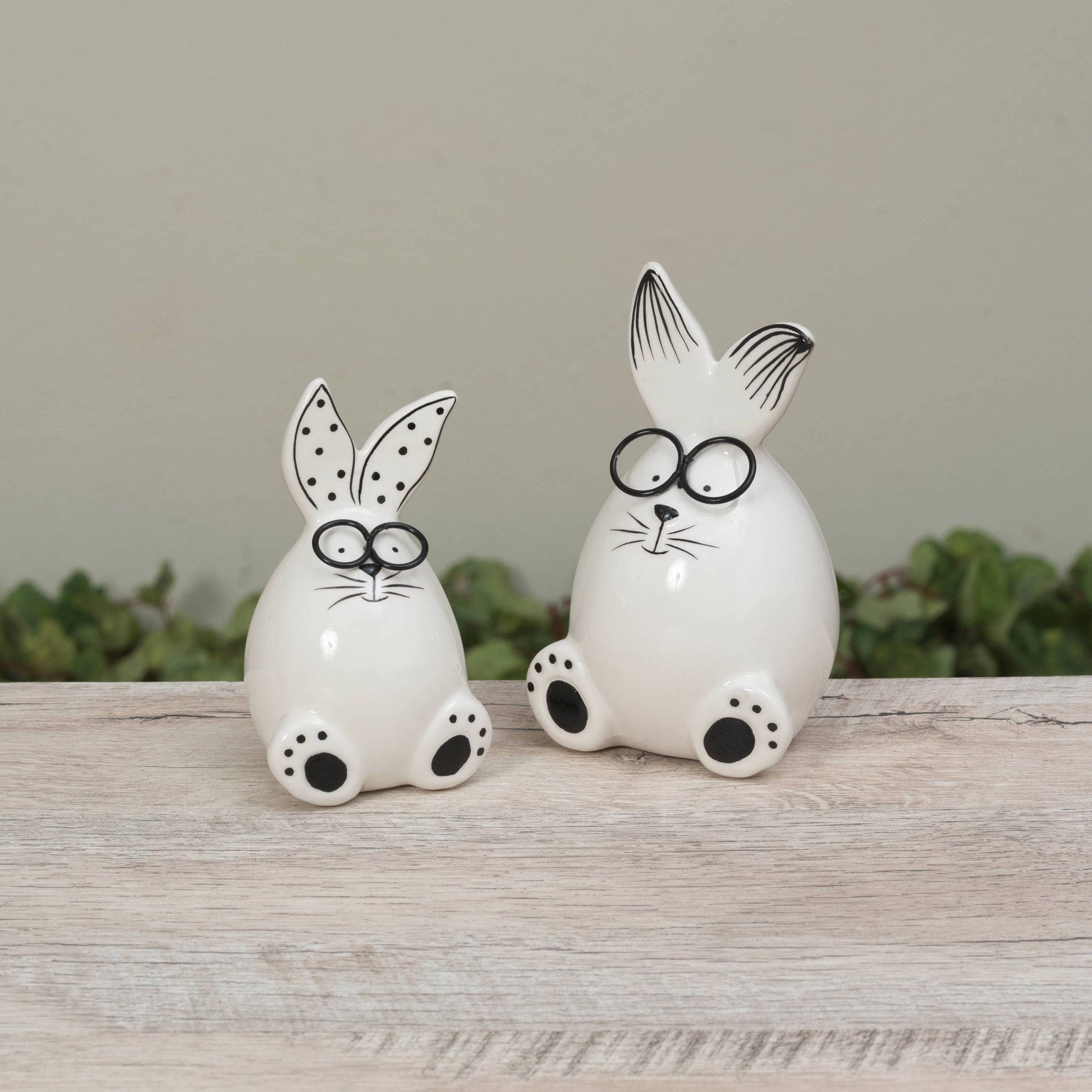 Two white ceramic rabbit figures with black glasses on a wooden surface.