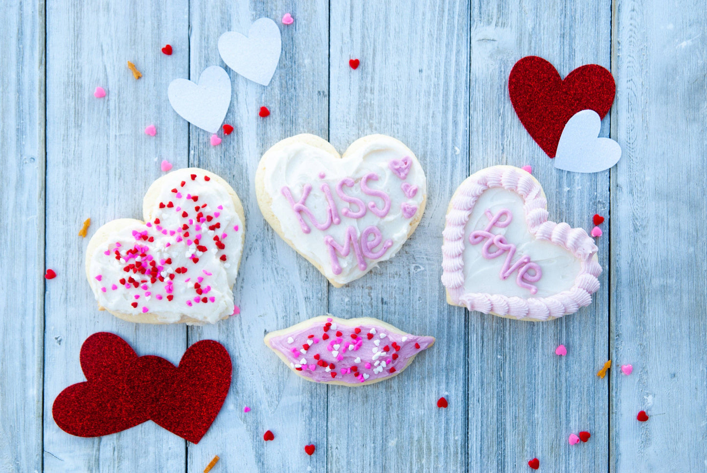 Heart-shaped cookies with 'Kiss Me' and 'Love' text on a wooden surface with heart decorations.