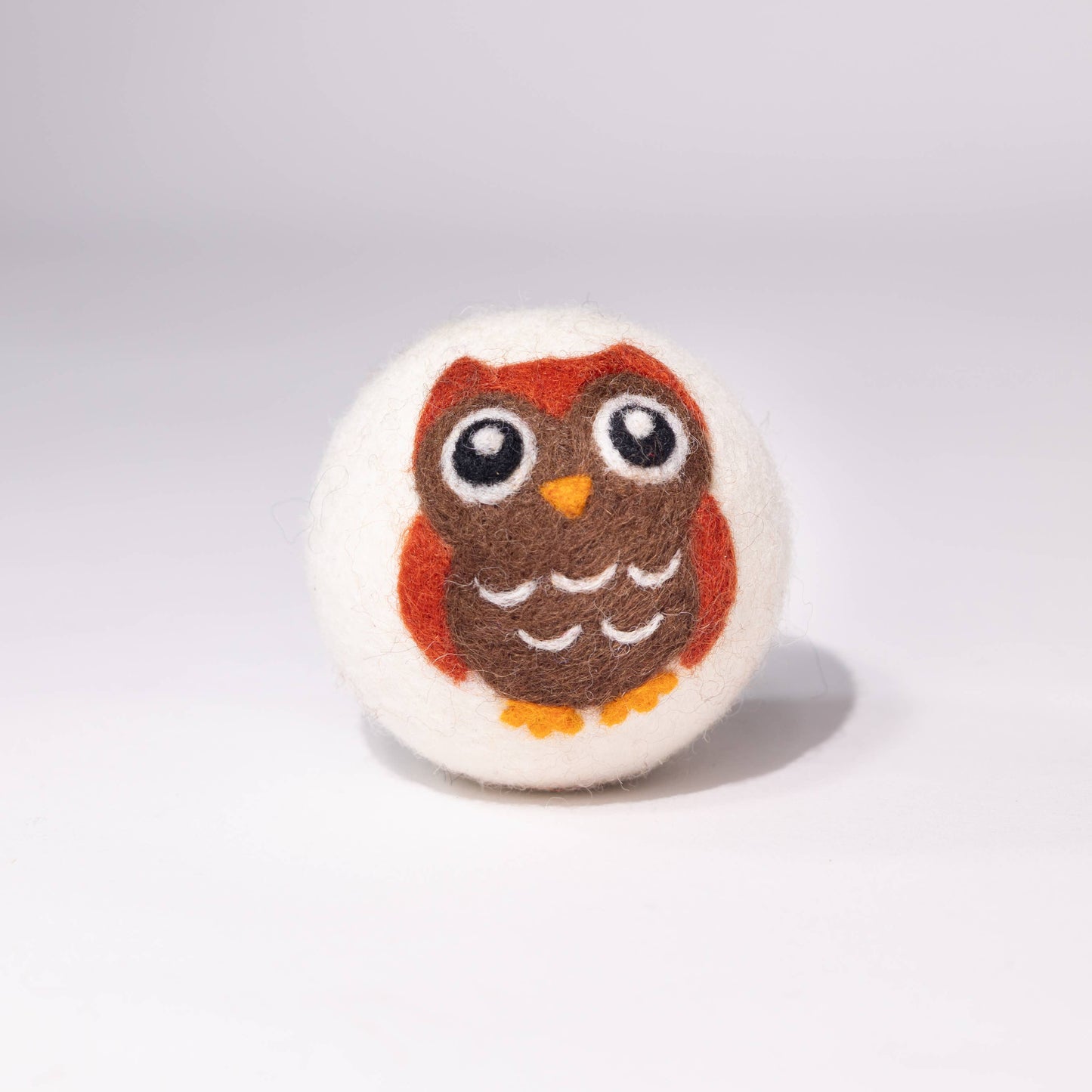 Round white wool dryer ball with an owl design on a light gray background