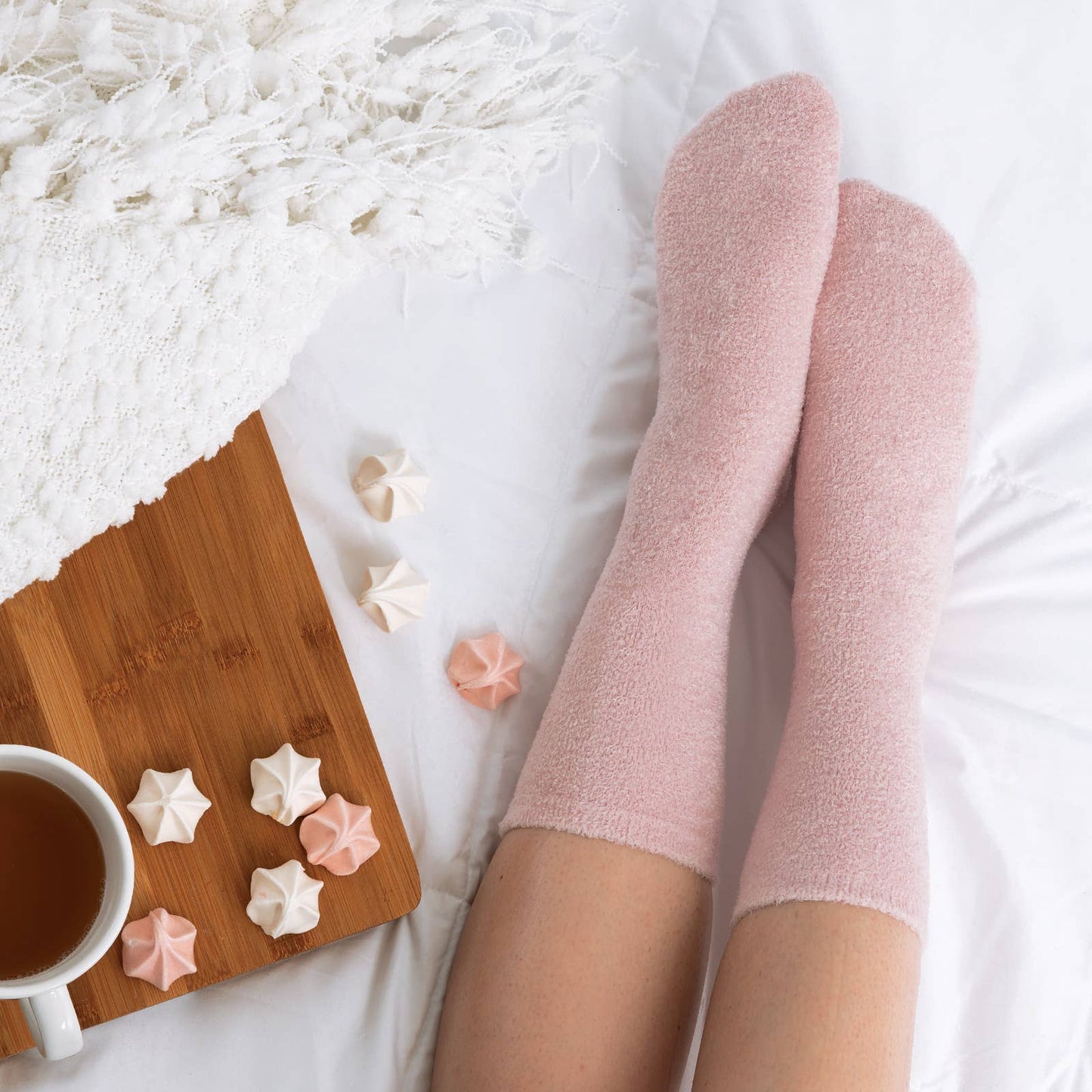 Person wearing pink socks with a cup of tea and cookies on a wooden board.