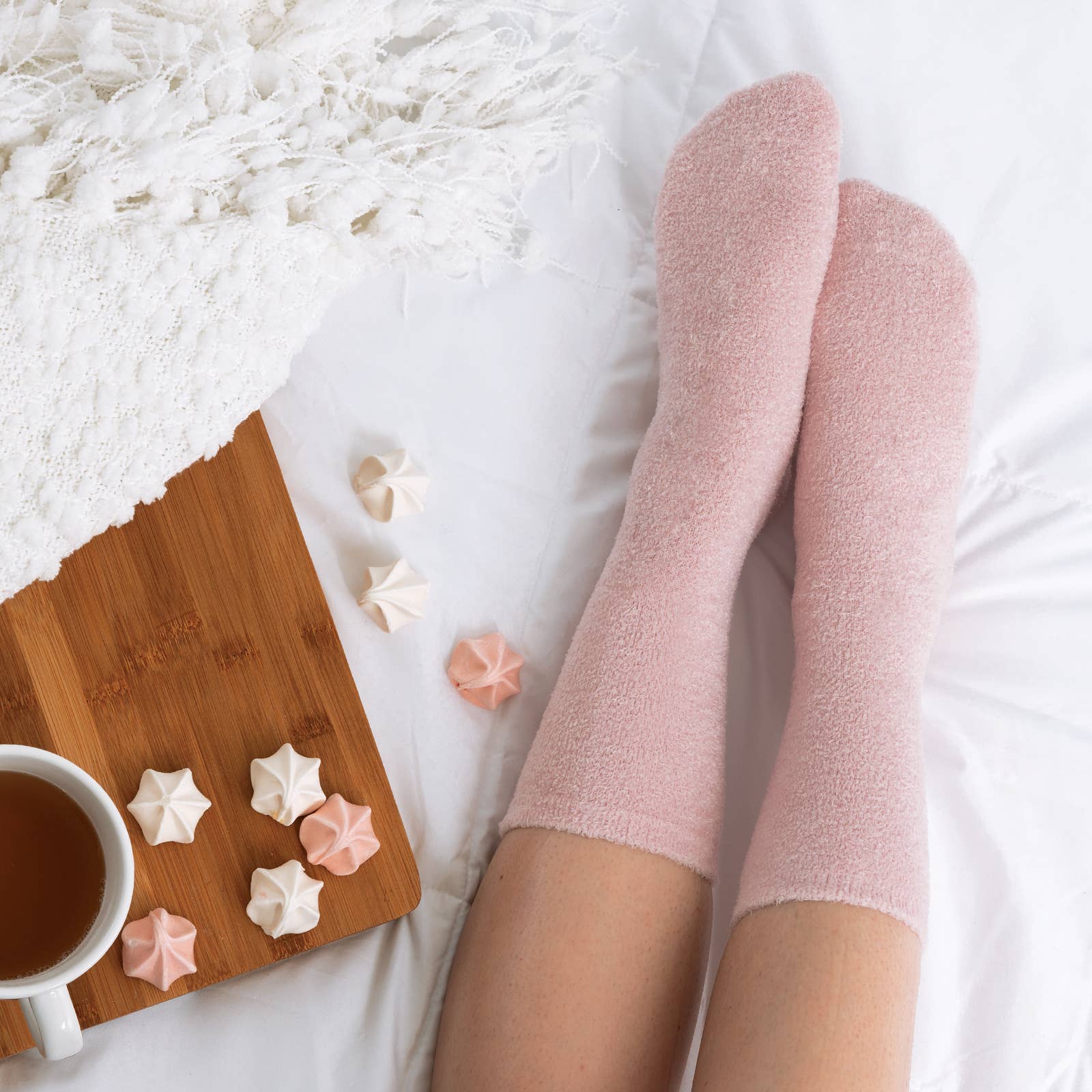 Person wearing pink socks with a cup of tea and cookies on a wooden board.