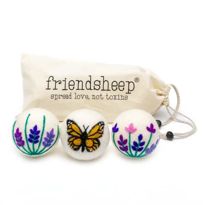 Three wool dryer balls with a butterfly and floral designs,  with a 'friendsheep' drawstring bag in the background.