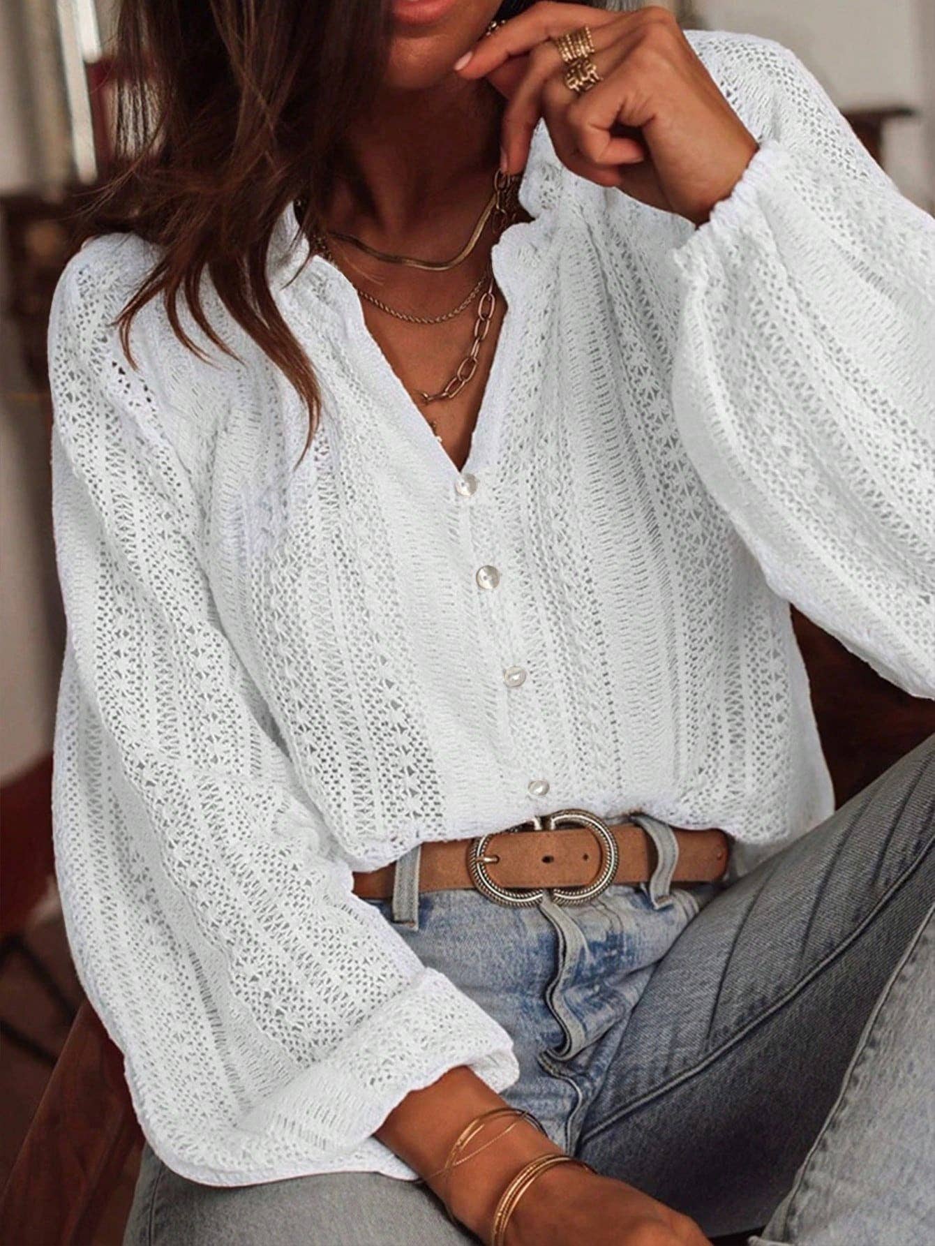Person wearing a white lace blouse with long sleeves and denim jeans.