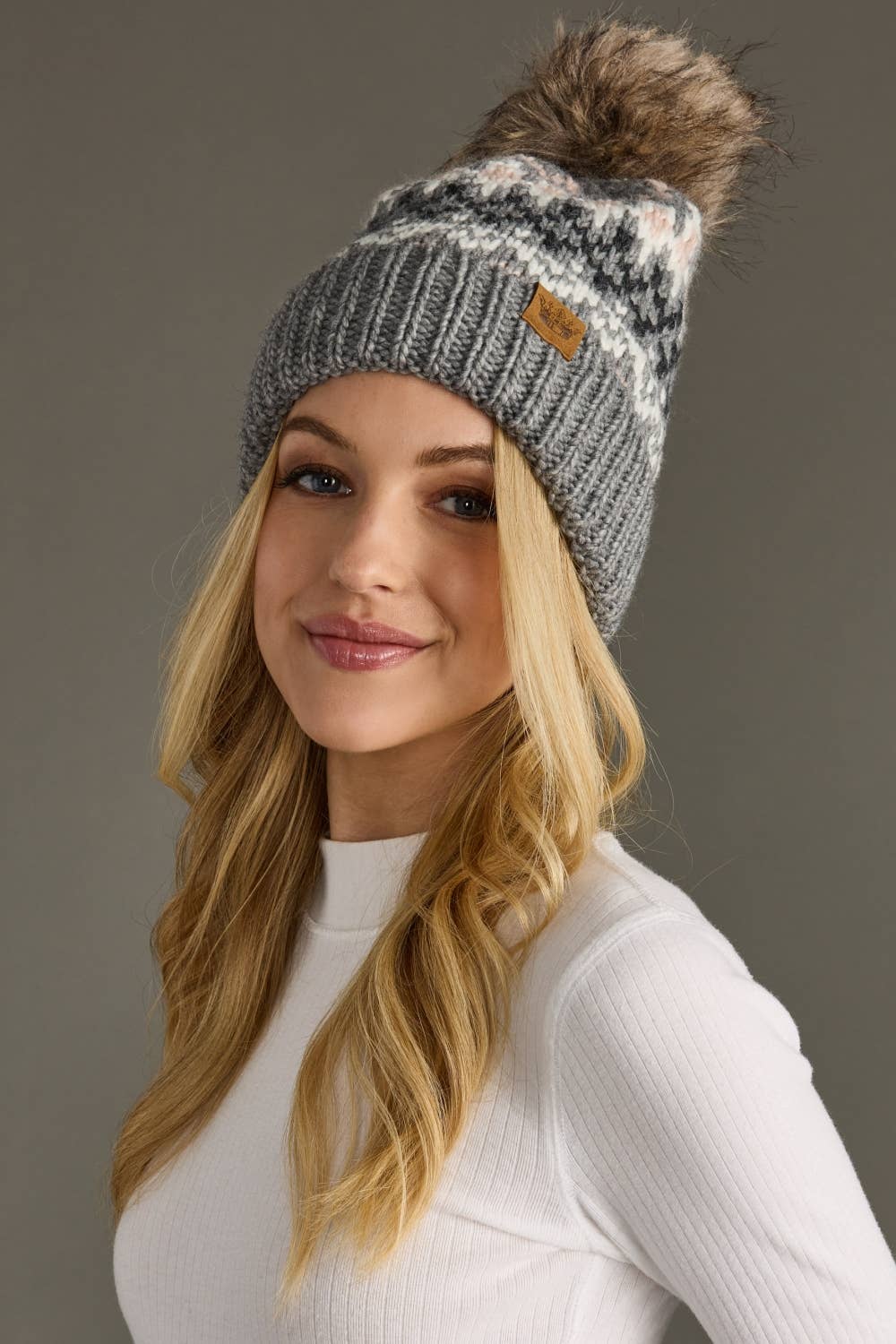 Woman wearing a gray knit beanie with a pom-pom on a gray background
