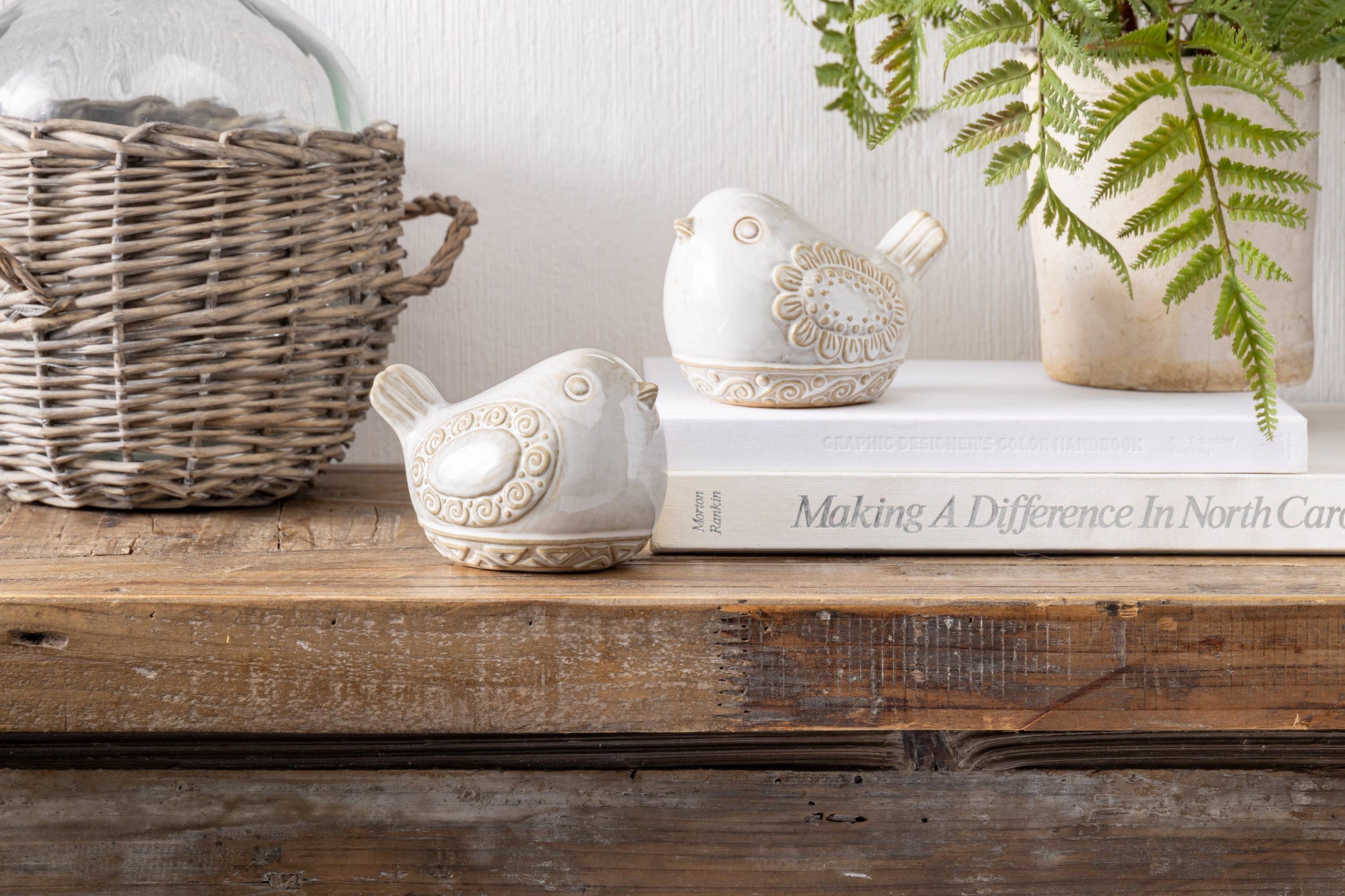 Decorative birds and a book on a wooden surface with a plant in the background